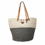 Natural sisal storage basket with leather handles holding blankets in a minimalist living room, handmade by Kenyan artisans by Asiliz.